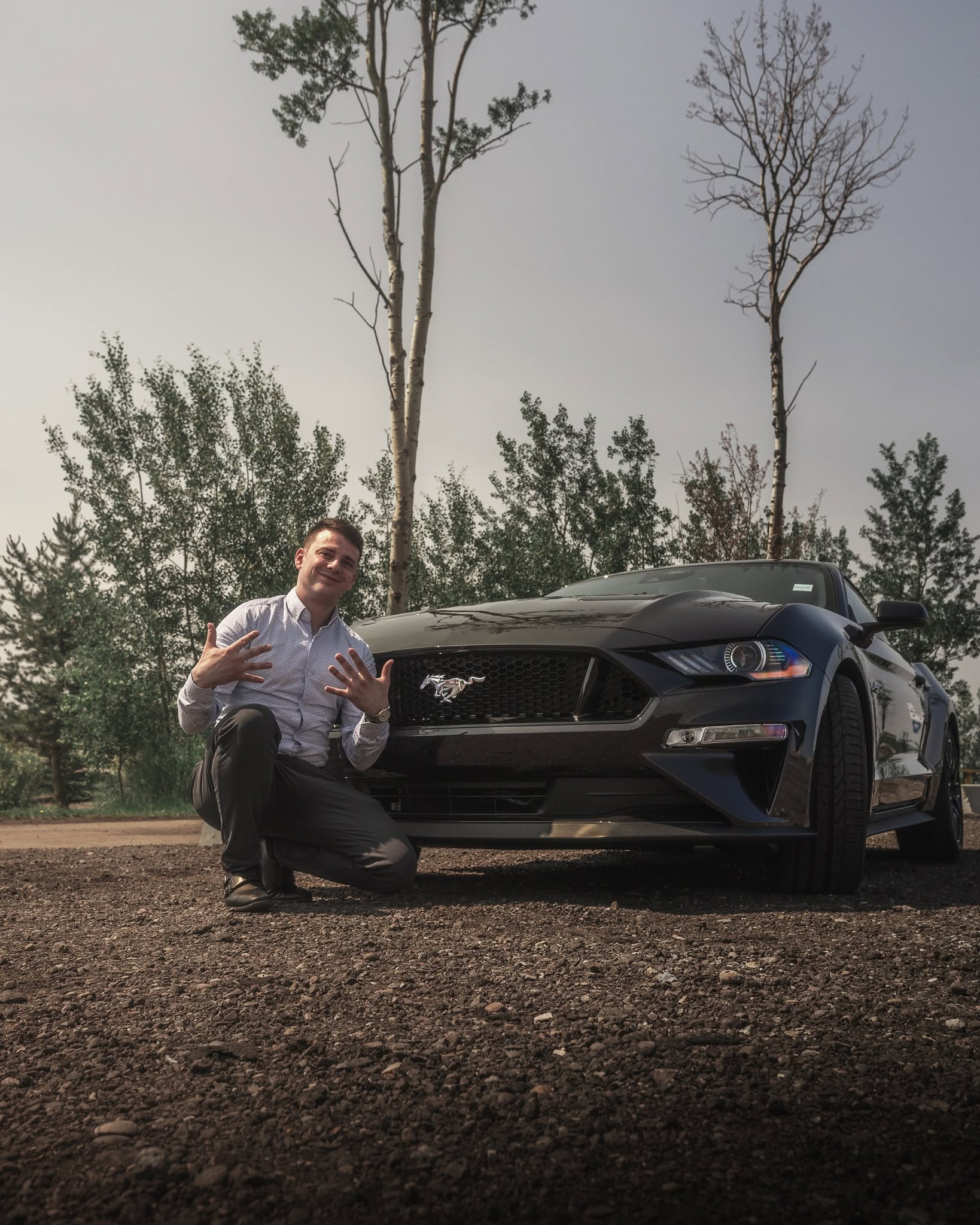 A Windsor Ford team member kneeling beside a Ford Mustang at golden hour