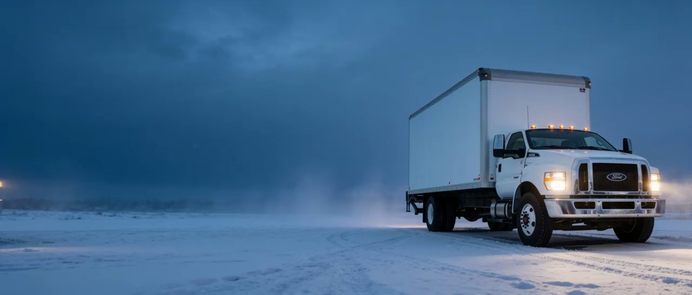 Ford F-750 commercial box truck at a snowy Grande Prairie lot at winter dusk